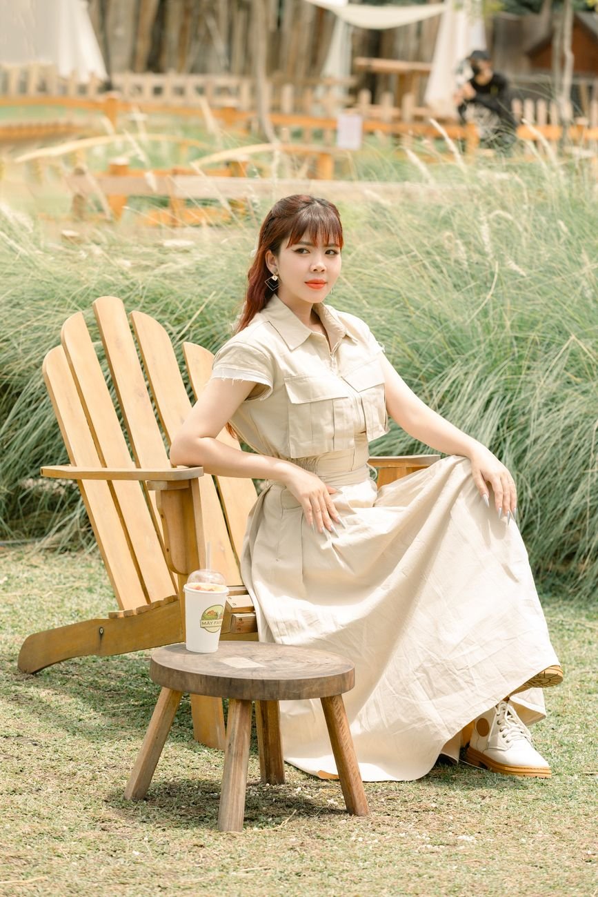 A woman in a beige dress sits in a chair outdoors on a summer day.