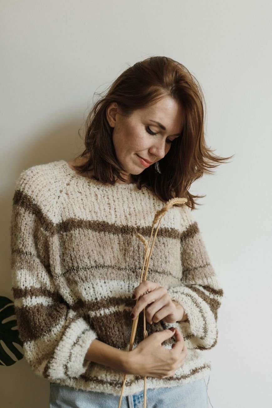 A woman in a striped knit sweater indoors, in soft light and neutral tones.